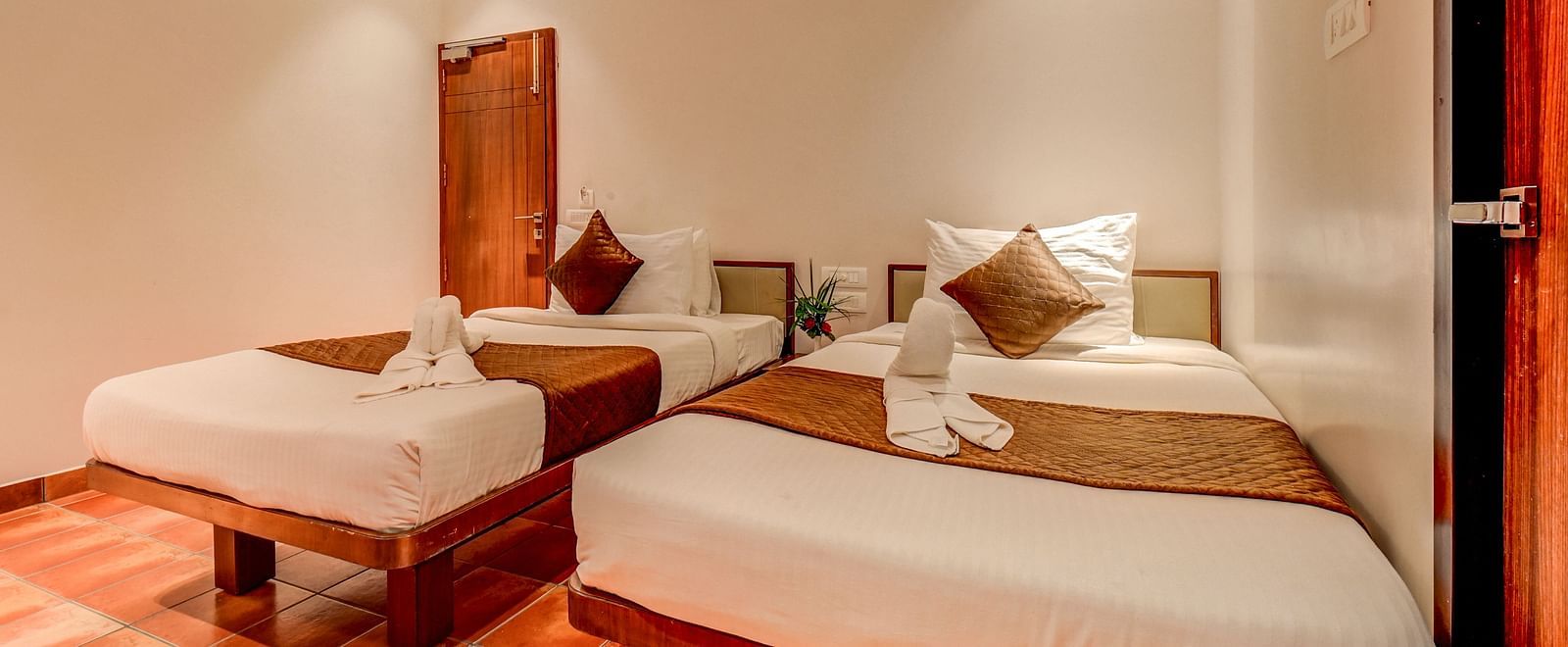 Two neatly made beds placed side by side, with a door to the side at Harigovinda's JNStay