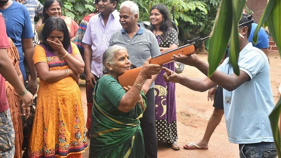 An old woman pointing a gun with a helper adjusting her aim - Evergreen County