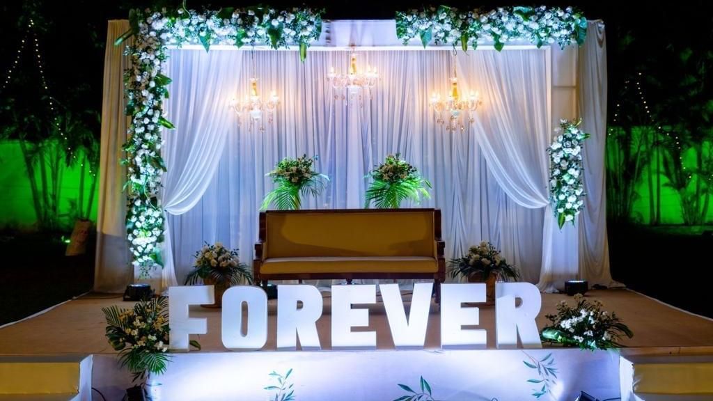 Chic wedding stage with sheer drapes, white florals, and a lit ‘FOREVER’ sign at Ilara Hotels & Spa, OMR, Chennai