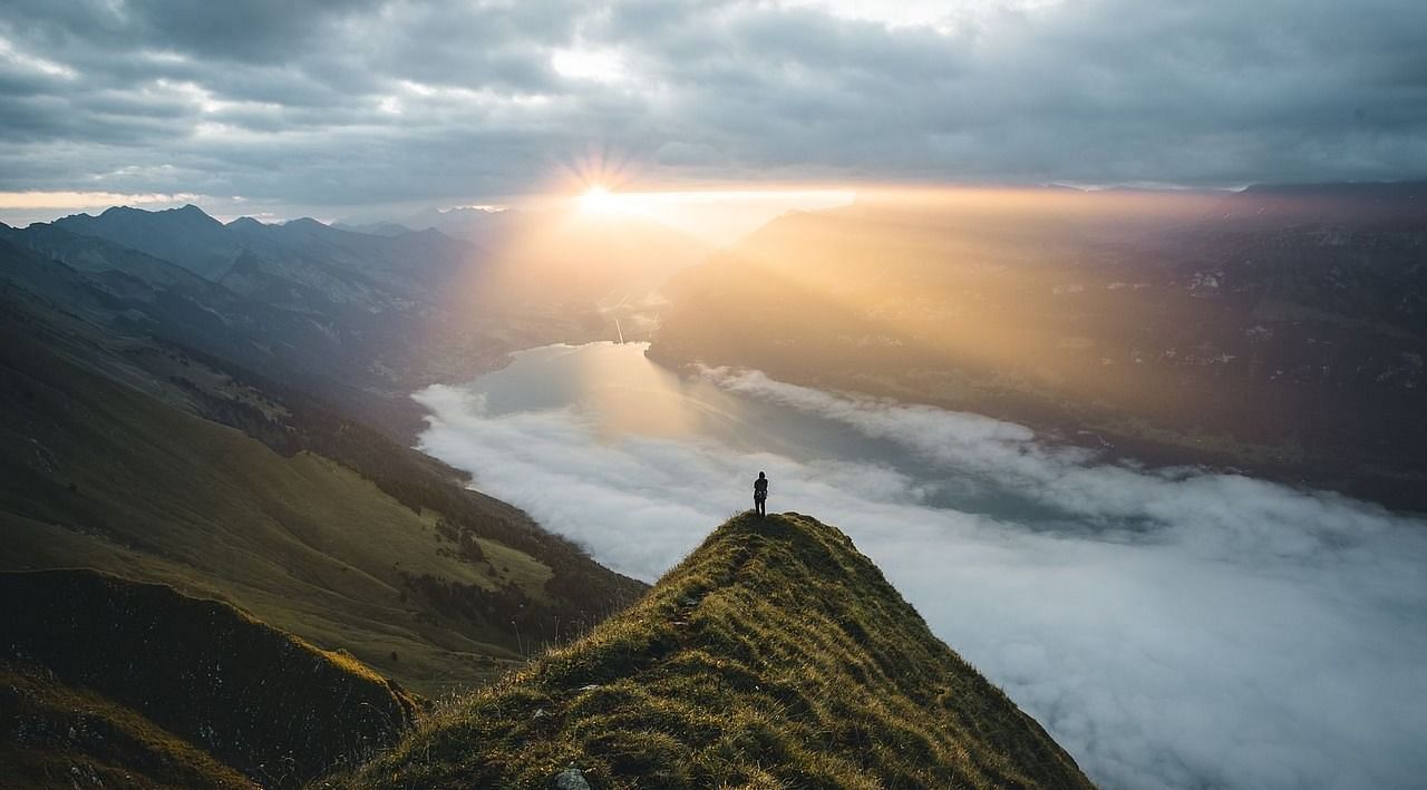 A lone hiker stands on a mountain ridge, overlooking a misty valley as the sun rises, casting golden rays across the landscape.