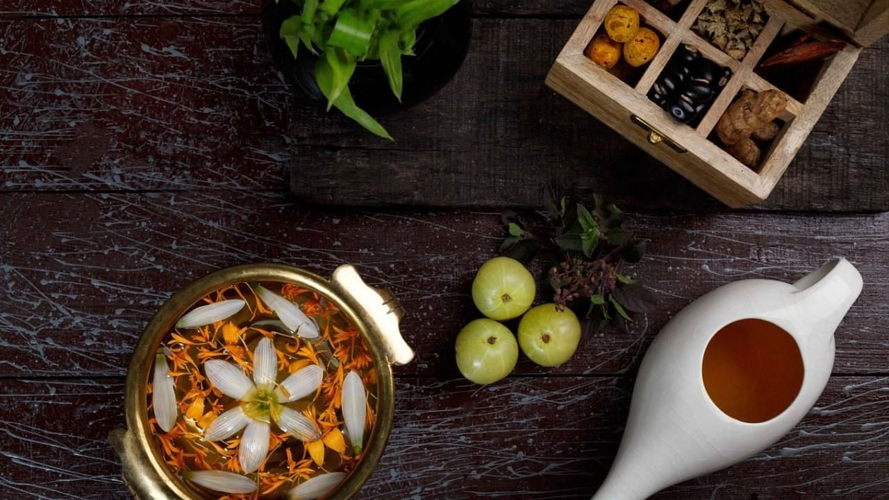 A top-down view of various food items and ingredients arranged on a dark wooden surface, including a bowl of curry, a white pitcher, and spices in small containers.