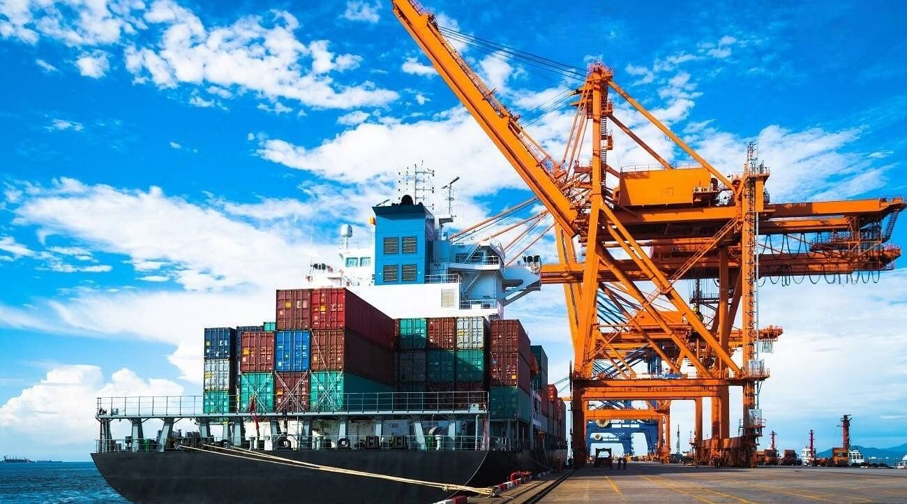 A cargo ship docked at a port being loaded with containers using large cranes.