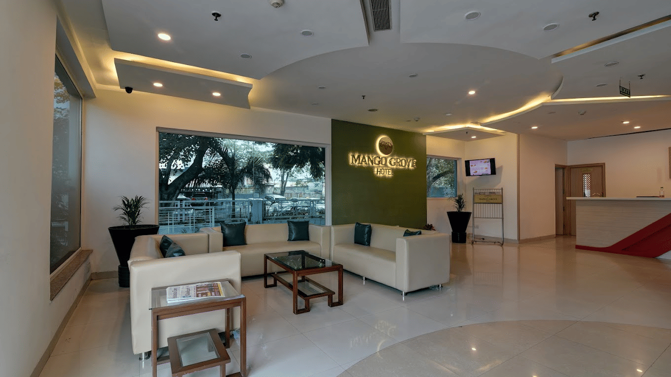 Lobby with wooden seating, a coffee table and a view toward the reception at Mango Grove Hotel.