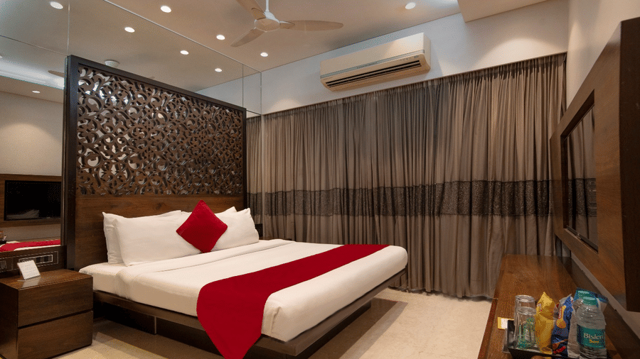 Bedroom at Theory9 - Premium Serviced Apts, Khar, featuring a carved wood headboard, white linens with a red runner, and wall-mounted TV.