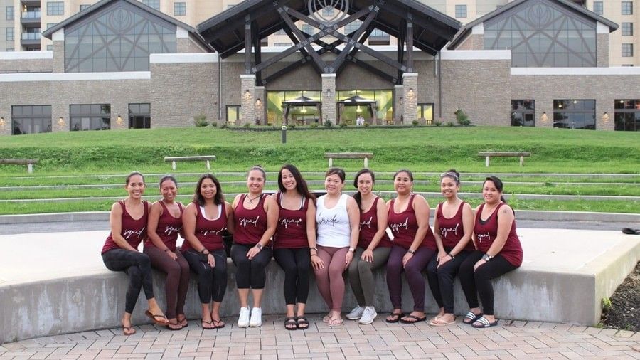 A group of 10 women sitting on a concrete surface in front of the facade of YO1 Longevity & Health Resorts