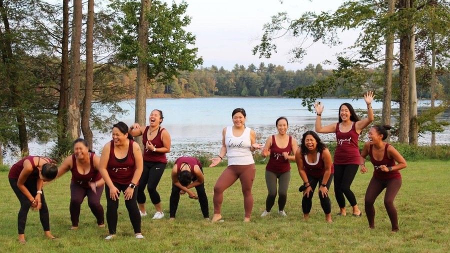  A group of nine women in maroon and white workout clothes standing near a lake and a forest at YO1 Longevity & Health Resort
