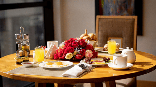 Wooden dining table set for a large breakfast with plates of food, orange juice, coffee cups, and fruit arranged on the table.