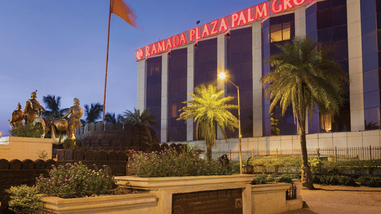 Exterior view of Ramada Plaza by Wyndham Palm Grove, showcasing its illuminated facade, palm-lined surroundings, and prominent city landmark setting.