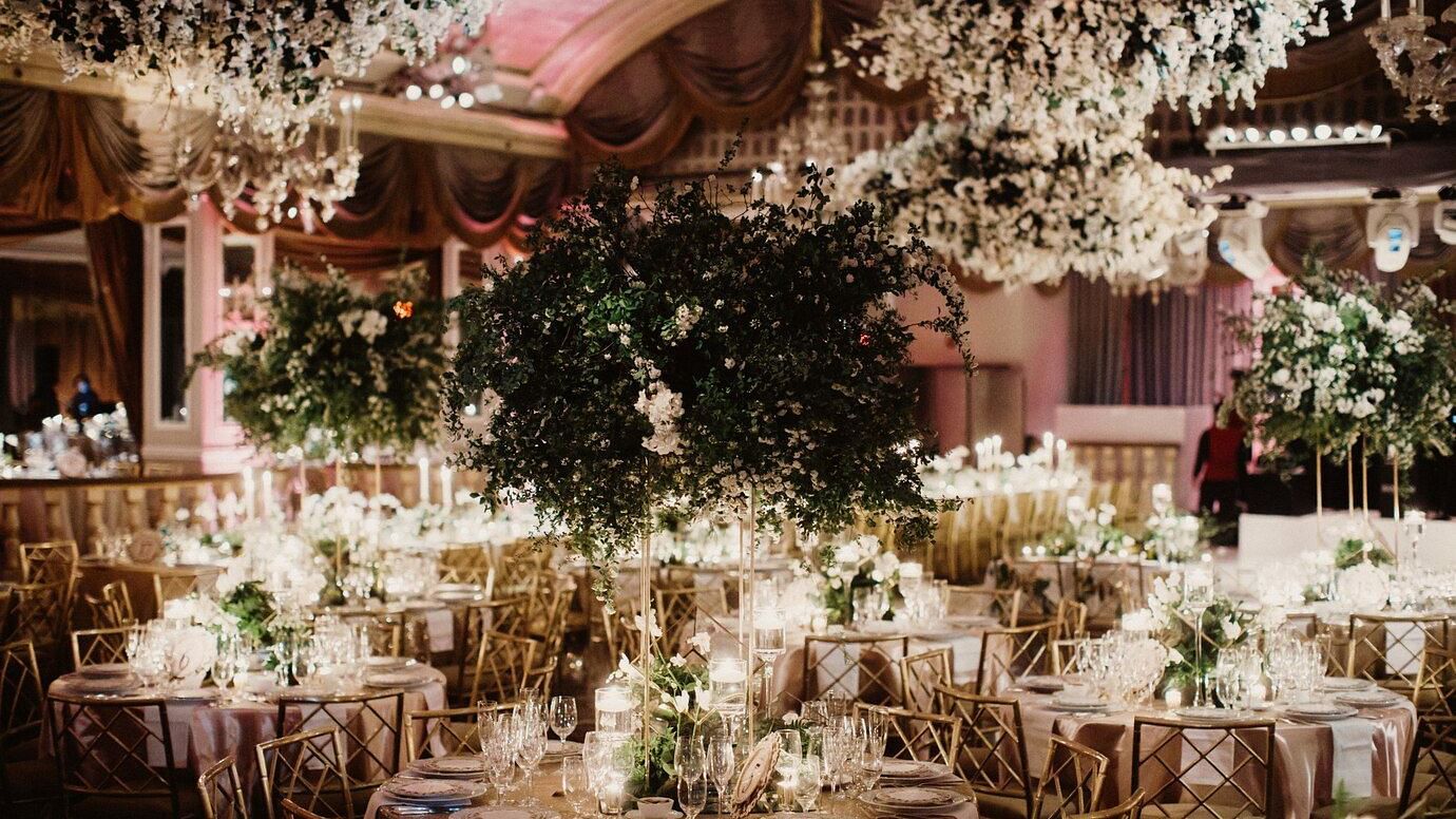 Elegant indoor wedding reception with floral decorations, chandeliers, and set tables, emphasizing a luxurious celebration.