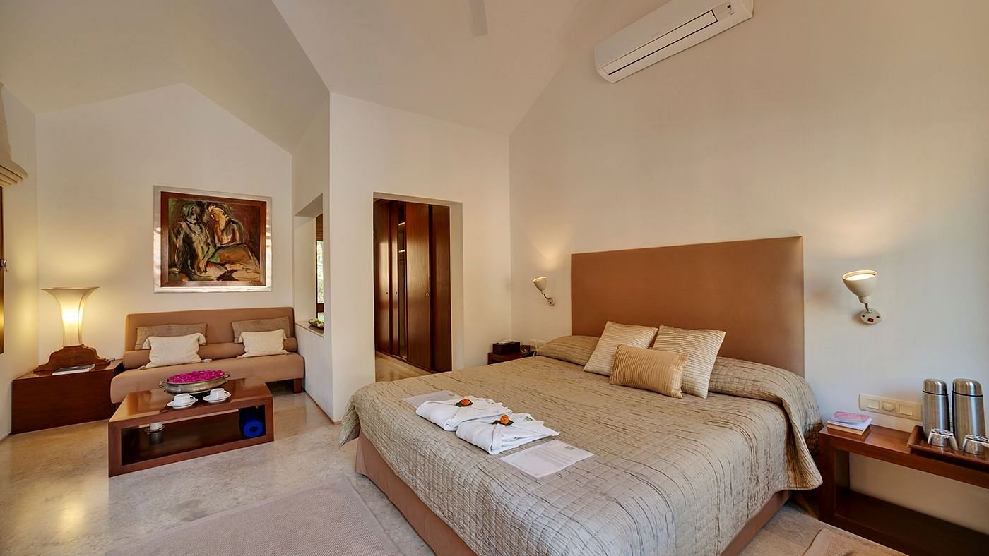 A wide angle image of a bedroom featuring a king size bed and a seating area with a cosy sofa - Shreyas Retreat