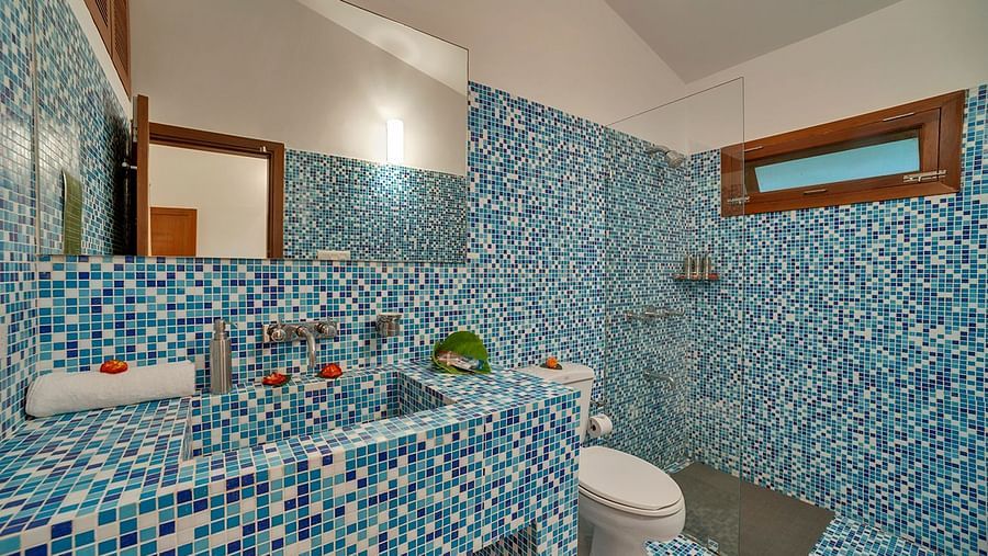A bathroom with blue mosaic tiles, a toilet, and a sink - Shreyas Retreat