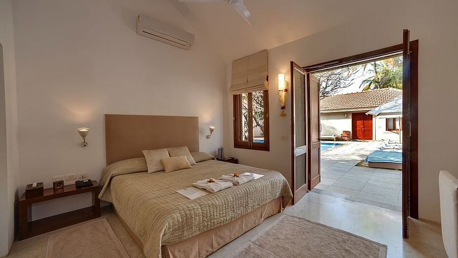 A bedroom featuring a king size bed, warm lighting and a door offering the access to a pool to unwind in - Shreyas Retreat