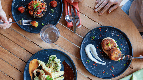3 plates of appetizers on a wooden table, with people eating using forks at YO1 Longevity & Health Resorts