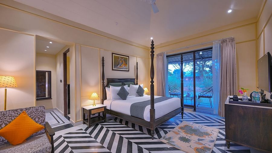 Luxury Suite Cottage with a four-poster bed, a living area with a patterned sofa and orange pillow, black and white chevron flooring, and a balcony - Singhvilas, Ranthambore