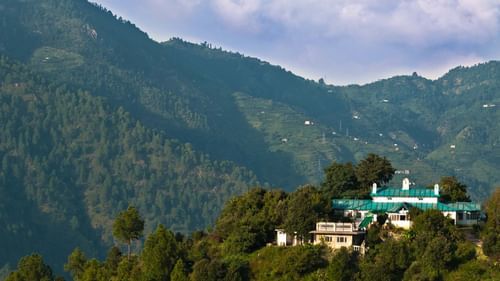 A magical view of the resort perched on the hill of Kumaon Hills covered with  trees during the day -Ramgarh Bungalows, Nainital.