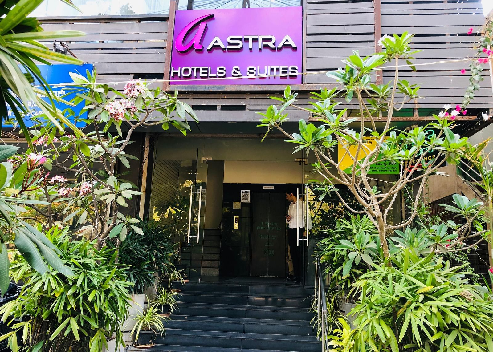 Entrance shot of Astra Hotels and Suites, HSR Sector 1 decorated with lot of plants and a sign board of the hotel.