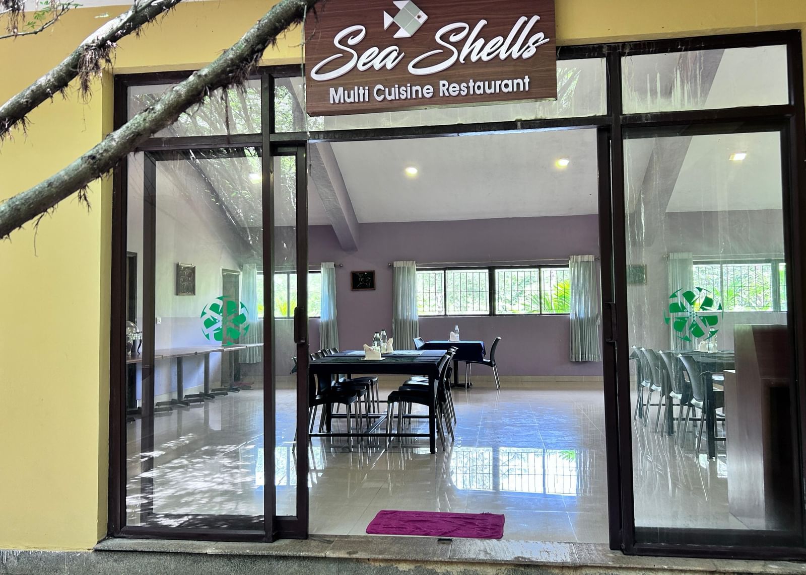 Glass entrance with 'Sea Shells Multi Cuisine Restaurant' signage at Paradise Wild Hills Resort, Kollur.