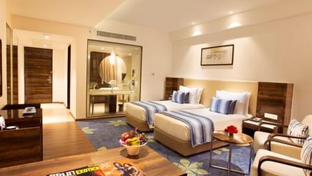 View of the room with two beds, two chairs, magazines on the table along with fruits and flowers.