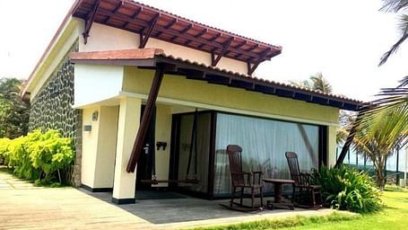 Charming cottage with a sloped roof, a lush green garden, and a patio.