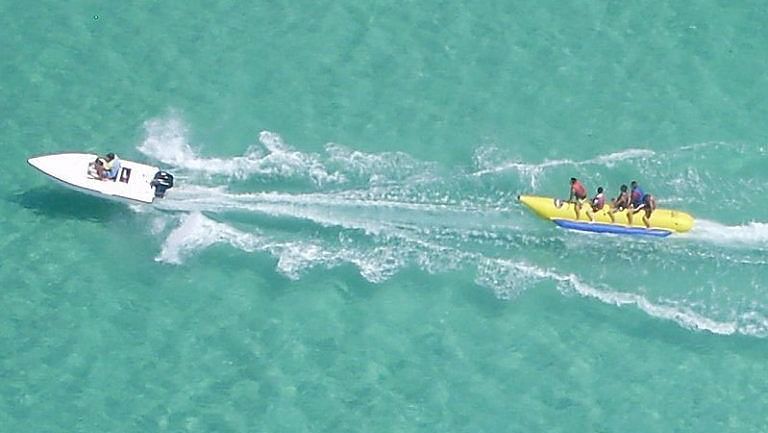 Excited riders on a banana boat whipped by a speedboat.