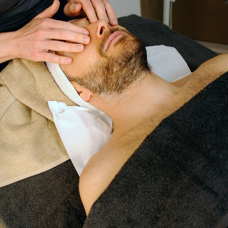 A man receiving facial massage from a masseur