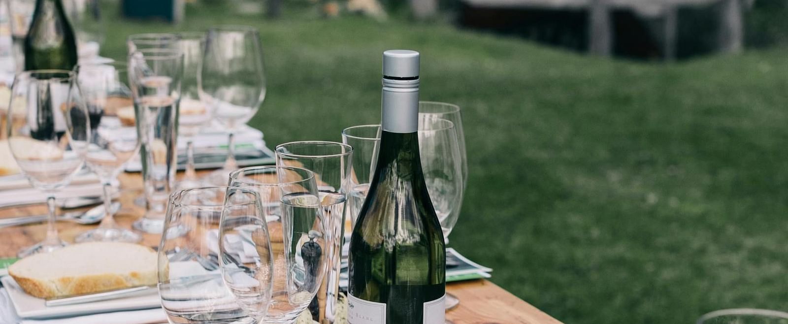 An outdoor dining table is elegantly set with wine glasses, plates, and bottles of wine.