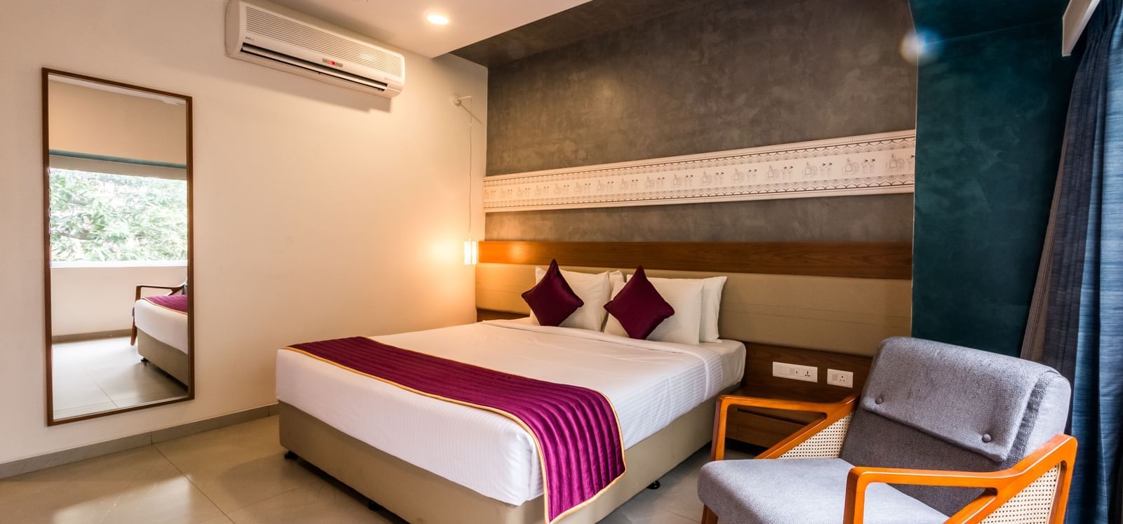 A spacious hotel room featuring a large bed, a full length mirror, and a comfortable armchair at Shilton Dee Cee.