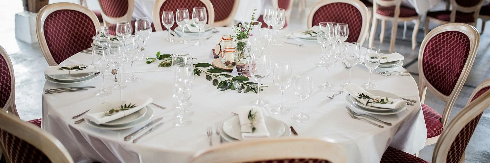 Tables set for a formal event with elegant white tablecloths and red chairs.