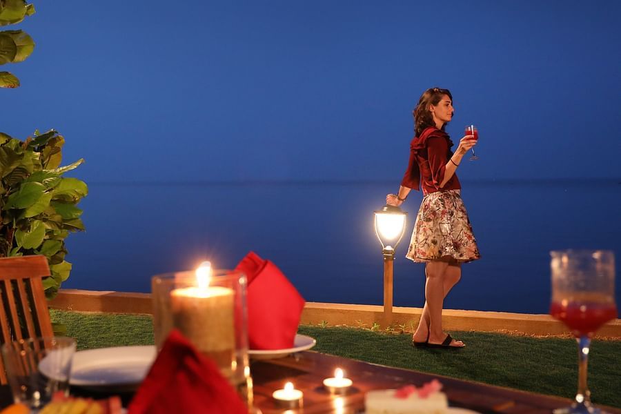 Romantic seaside dinner with candlelit table, gourmet food, and a woman gazing at the ocean under a deep blue evening sky at Uday Backwater Resort