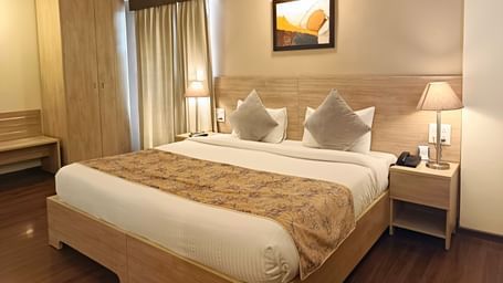 Plush bed with a couple of lamps lit on both sides on the nightstands inside warmly lit premium studio at Starlit Suites, Shirdi