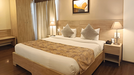 A plush bed with lamps lit on both sides on the nightstands inside a warmly lit Premium Room at Starlit Suites, Shirdi.