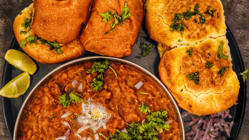 A plate of pav bhaji served with bread rolls, onions, lemon slices, and chutney.