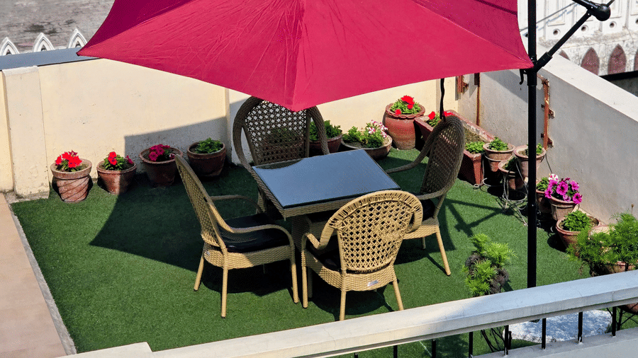 Hotel Exotic, Amritsar features an outdoor seating area with tables, chairs, a red canopy and surrounding greenery.