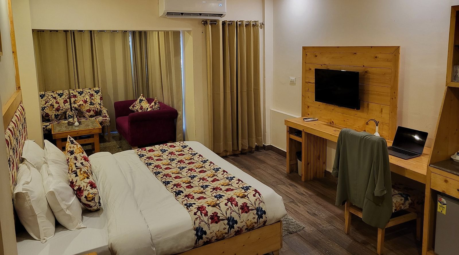 A well-lit hotel room with a bed, colourful cushions, a TV, and a work desk at Dagshai Manor Kasauli - Inde Hotels.