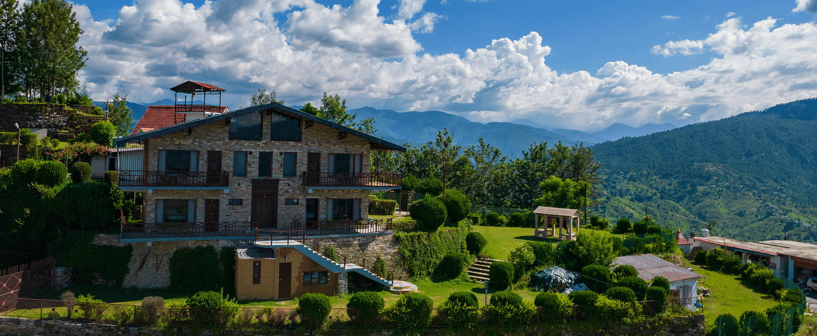 A charming villa surrounded by lush greenery and set against the backdrop of rolling hills and blue skies. - Blusalzz Homes The Himalayan Bungalow, Almora