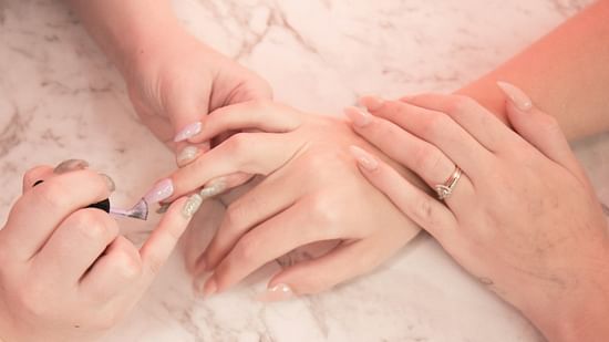A therapist giving a manicure therapy for a clients hand, showcasing a pink tint in the image.