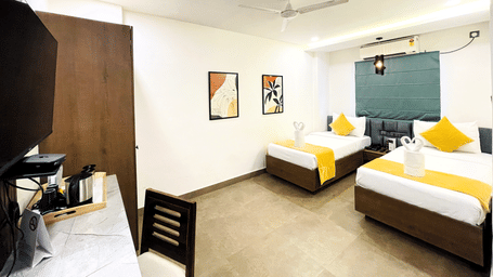 Twin bed room at Hotel Kyzen Smart Stays Madhapur with yellow accent bedding, teal headboard wall panel, wooden wardrobe, work desk, and warm ceiling lighting.