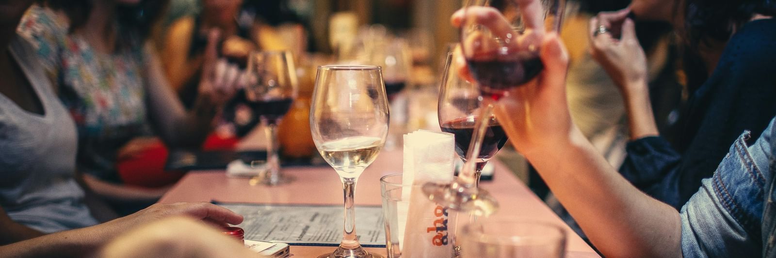 A long row of people seated at a table, having drinks, visibly wine, and bar snacks.