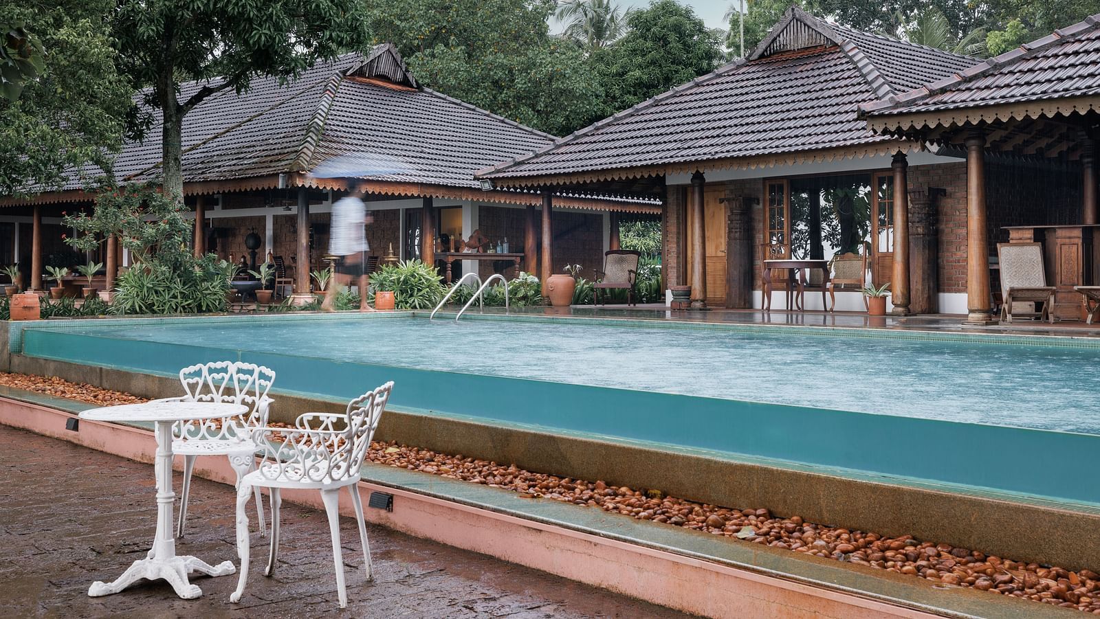 A shot of the pool with chairs and table near it and the restaurant in the background - BluSalzz Villas - Muhamma Resort, Alleppey