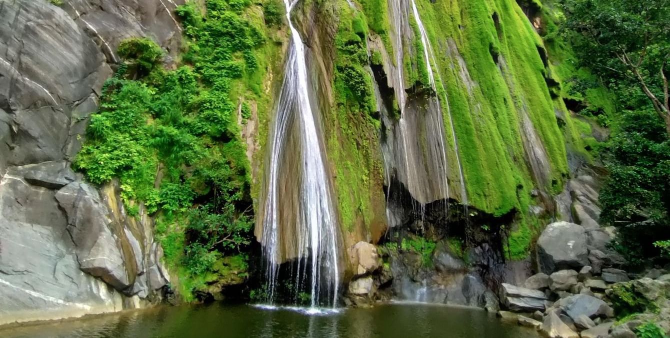 Bheel Beri Waterfalls in Rajasthan featuring water cascading down the rocky mountain surrounded by plants. At the bottom there is a pond where water gets collected.