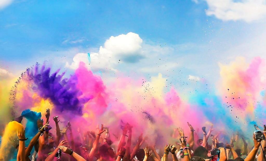 Joyful group celebrating Holi with vibrant colors against a bright, clouds on the sky