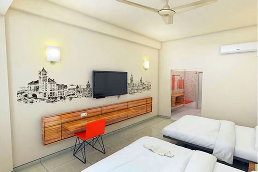 alt-text A hotel room with twin beds, white bedding, a flat-screen TV on a wooden console, a single red chair, and wall art depicting historic buildings.