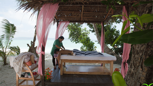 A masseuse massaging a client under a canopy by the beach in spa at Havelock.