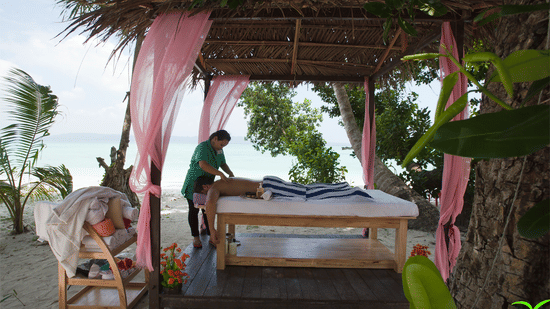 A masseuse massaging a client under a canopy by the beach in spa at Havelock. a