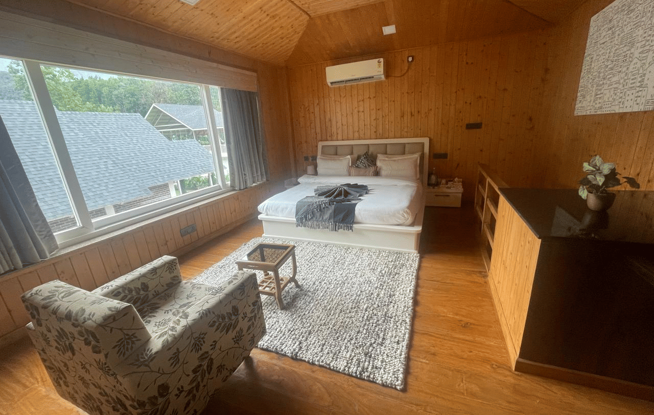 An angled shot of a bedroom with large windows, a comfortable chair, and a white rug at Megha Resort & Villas, Dehradun.