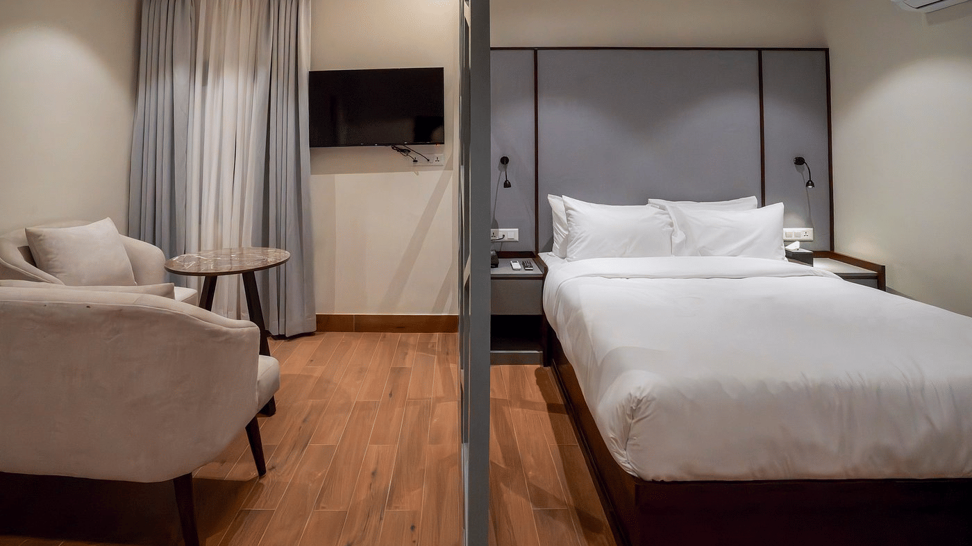 Guest room with a double bed, grey upholstered headboard, armchairs with a round table, wall-mounted TV and wooden flooring at Ila Comfort, Baglung.
