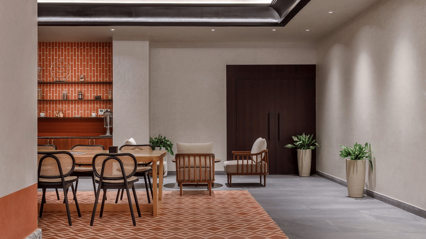 Tea and coffee corner with a terracotta-tiled wall, open shelves, cane dining chairs and a patterned tiled floor at Ila Resort, Maulakali.