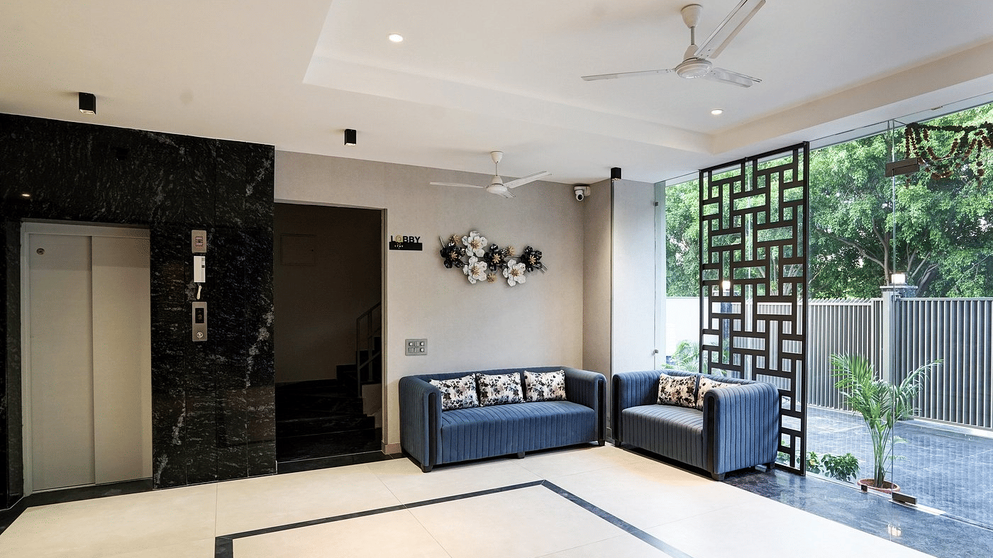 Lounge area of Lime Tree Hotels & Service Apartment Private Limited featuring a decorative jali partition, a sofa, and a ceiling fan.