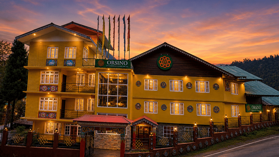 A facade of the Orsino Khangri Karpo Retreat & Spa, Lachung building from the road at sunset with several flags flying in front of the entrance.