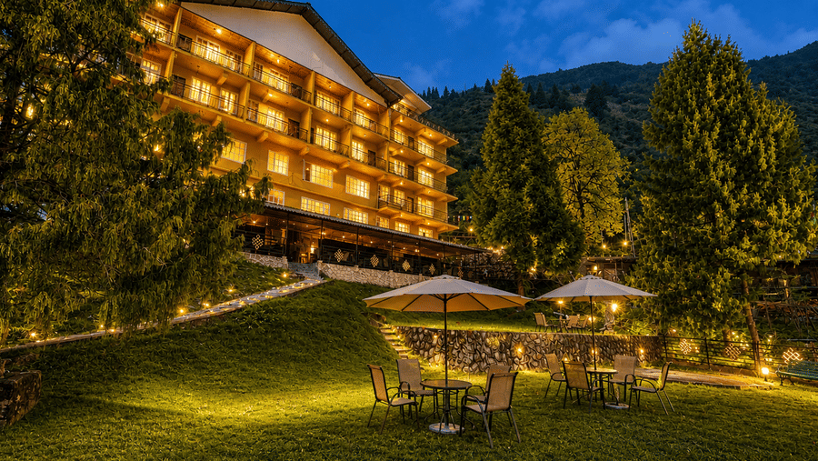 An evening view of the garden at Orsino Khangri Karpo Retreat & Spa, Lachung with illuminated paths and seating arrangements under umbrellas.